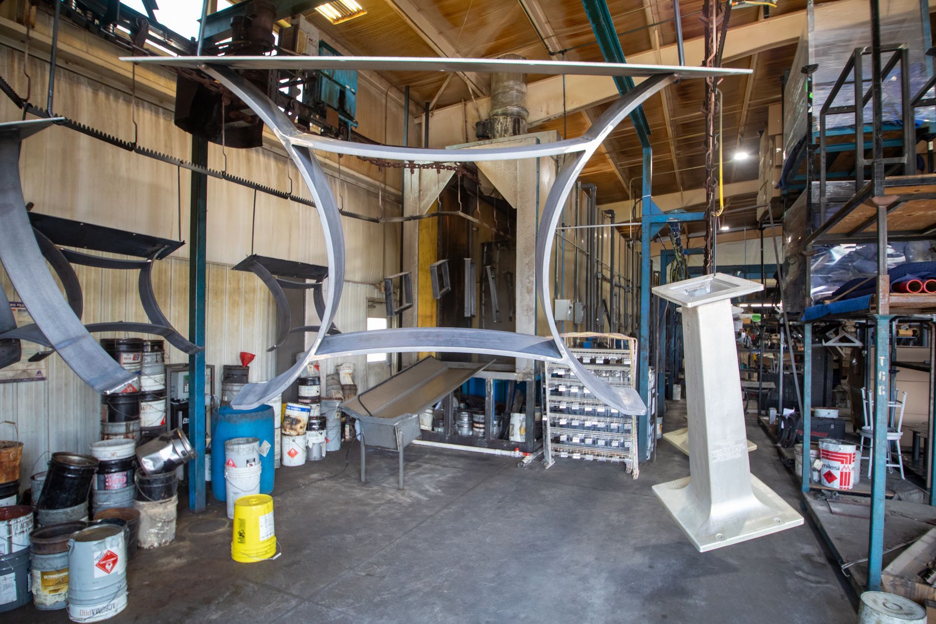 Metal table frame hanging in a workshop, surrounded by paint cans and equipment.