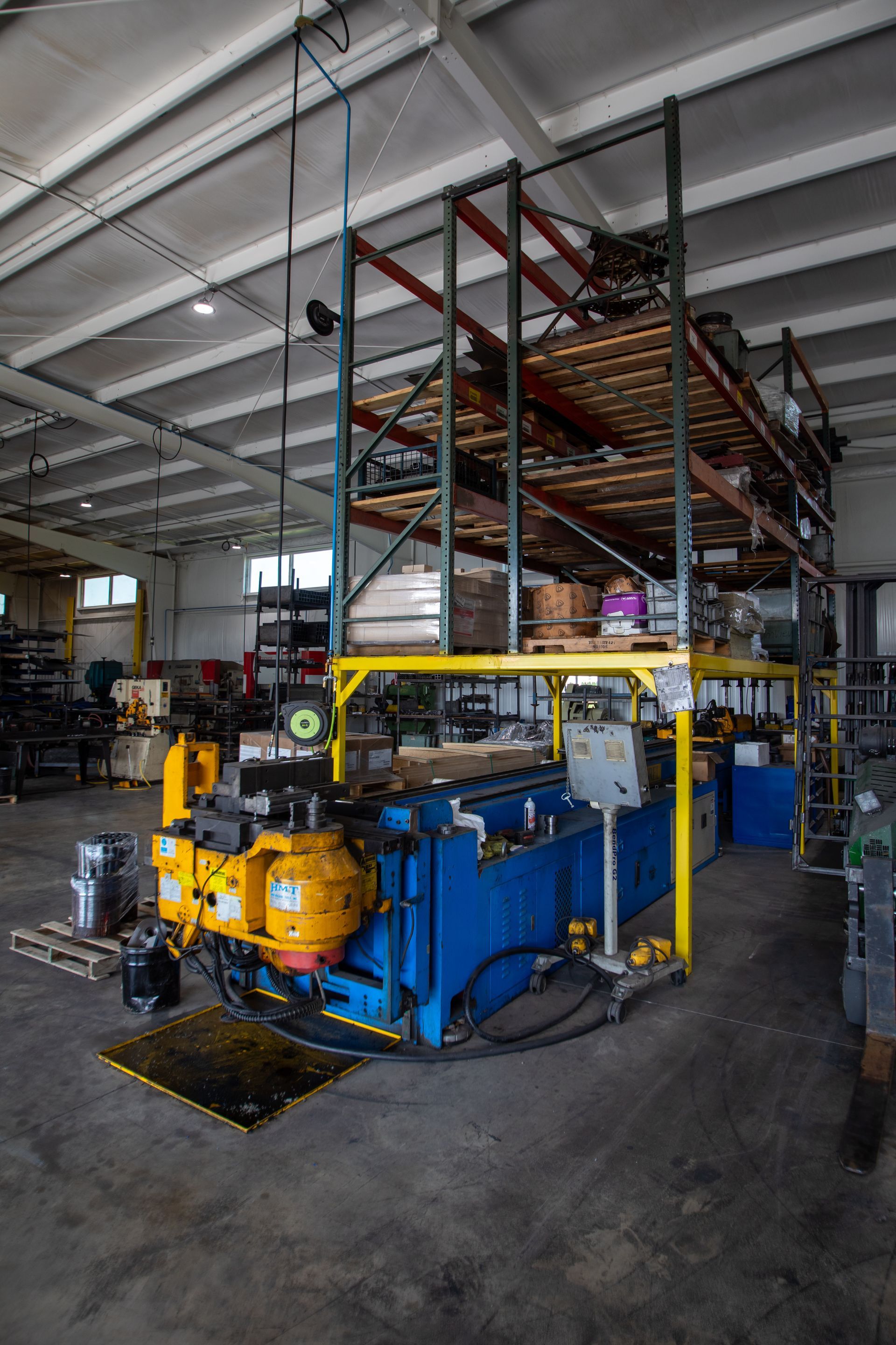 Large industrial machine in a warehouse, with shelving overhead. Blue and yellow machinery.