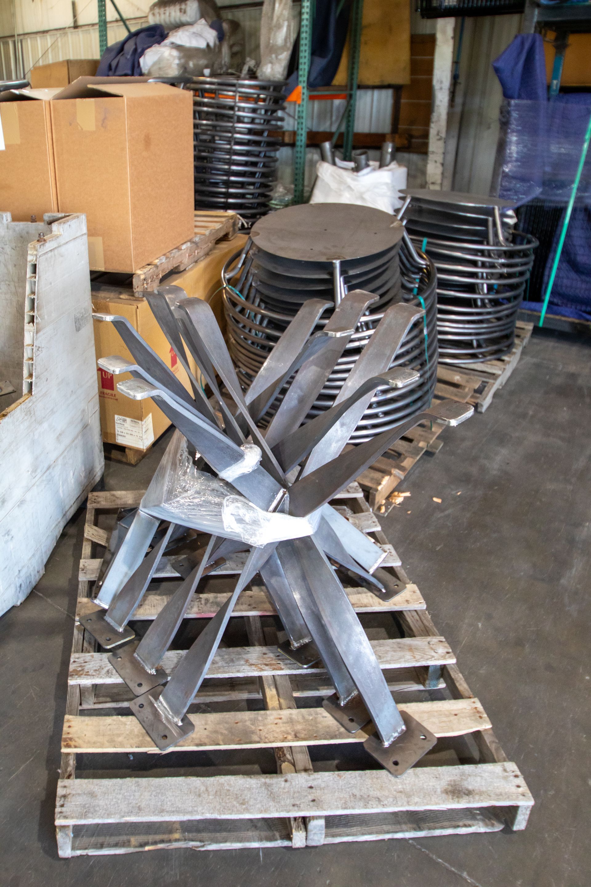 Metalwork components on a pallet: Star-shaped base and circular, stacked metal rings, inside a warehouse setting.