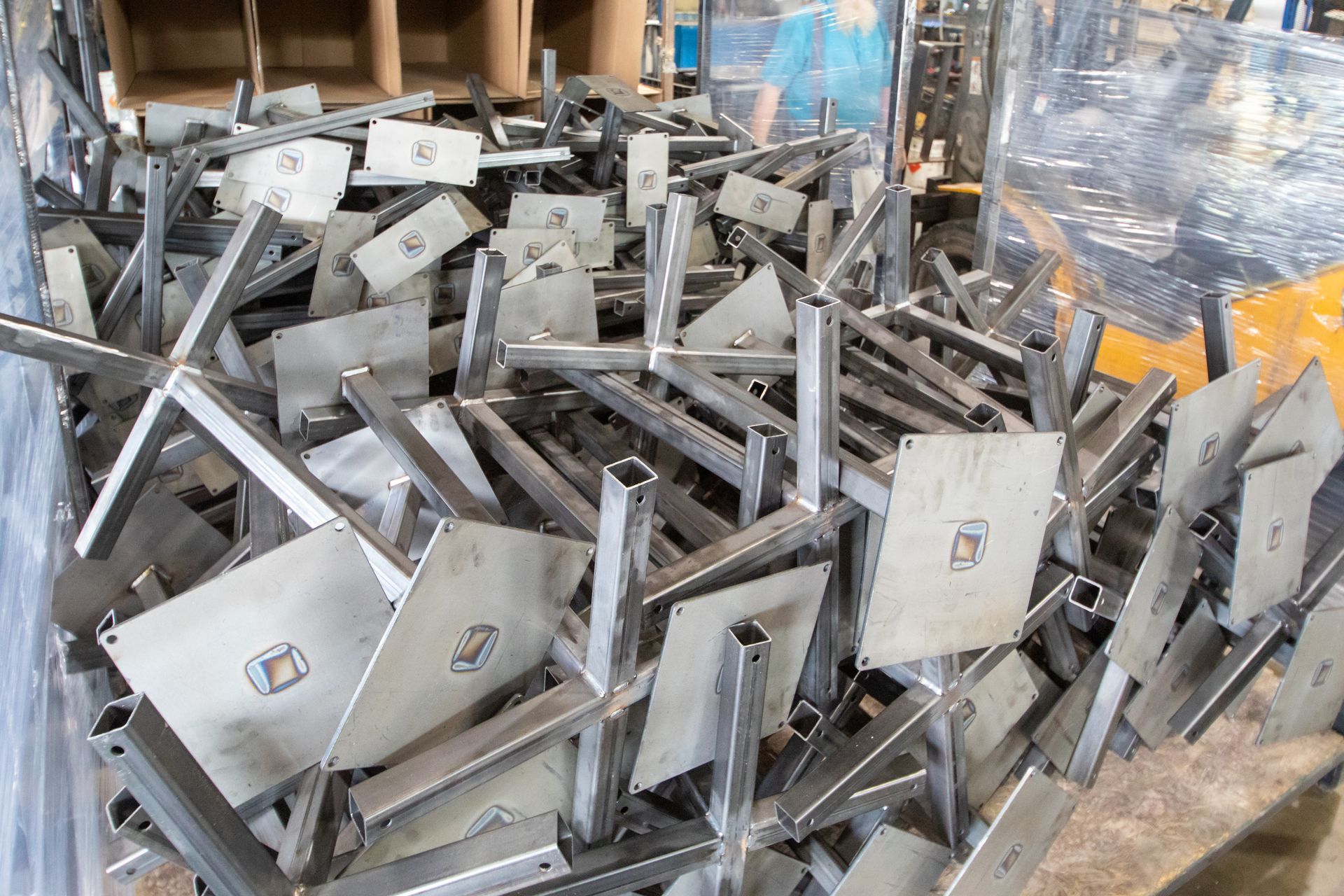 Pile of silver metal table bases in a warehouse, some with round stickers.