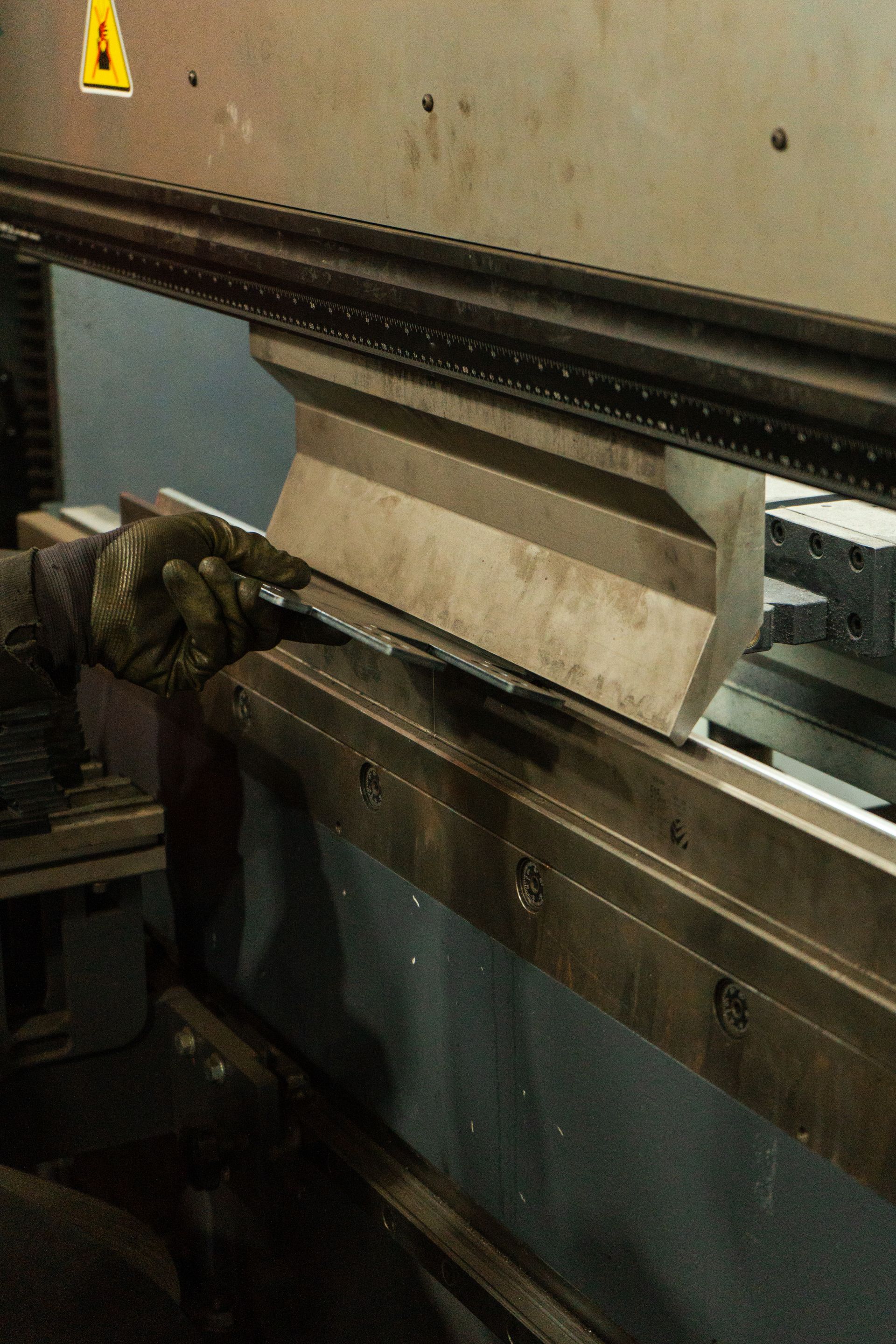 A person wearing work gloves bends metal using an industrial press brake machine in a workshop.