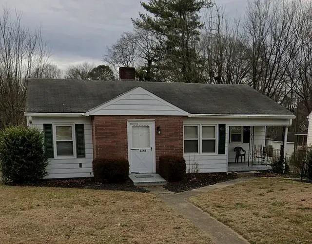 Small single-story white house with a red brick center, front walkway, and leafless trees in front