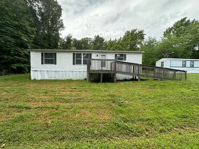 Single-story white mobile home with a wooden ramp in a grassy yard under cloudy skies