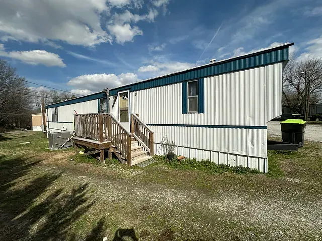White mobile home with blue trim and porch on a gravel lot under a cloudy sky