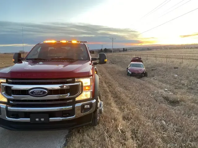 A red tow truck is driving down a road next to a field.