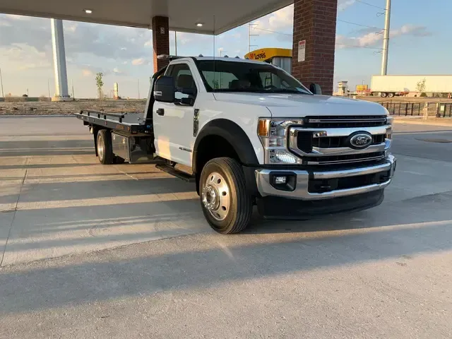 A white tow truck is parked in front of a gas station.