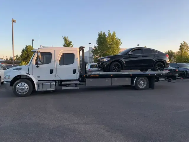 A tow truck is carrying a black car on the back of it.
