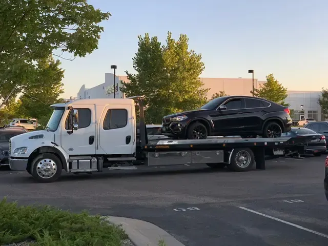 A tow truck with a black car on the back is parked in a parking lot.