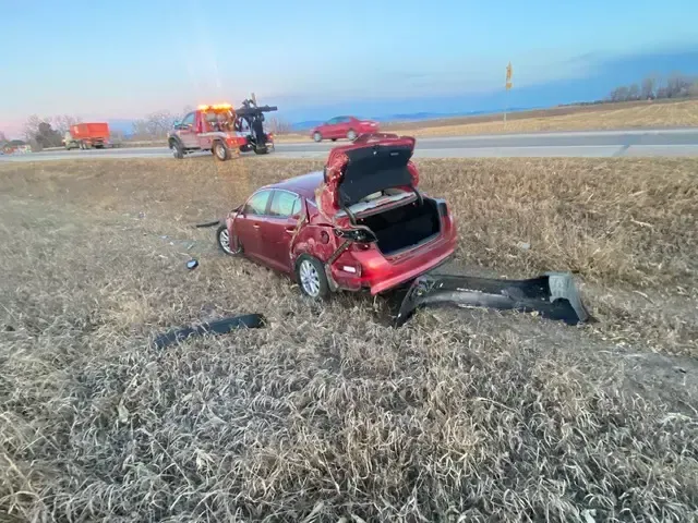 A red car is laying in the grass on the side of the road.