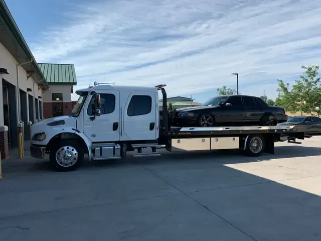 A tow truck with a car on the back is parked in a parking lot.