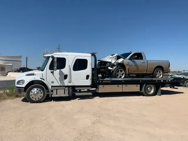 A tow truck is carrying a pickup truck with a wrecked car on top of it.