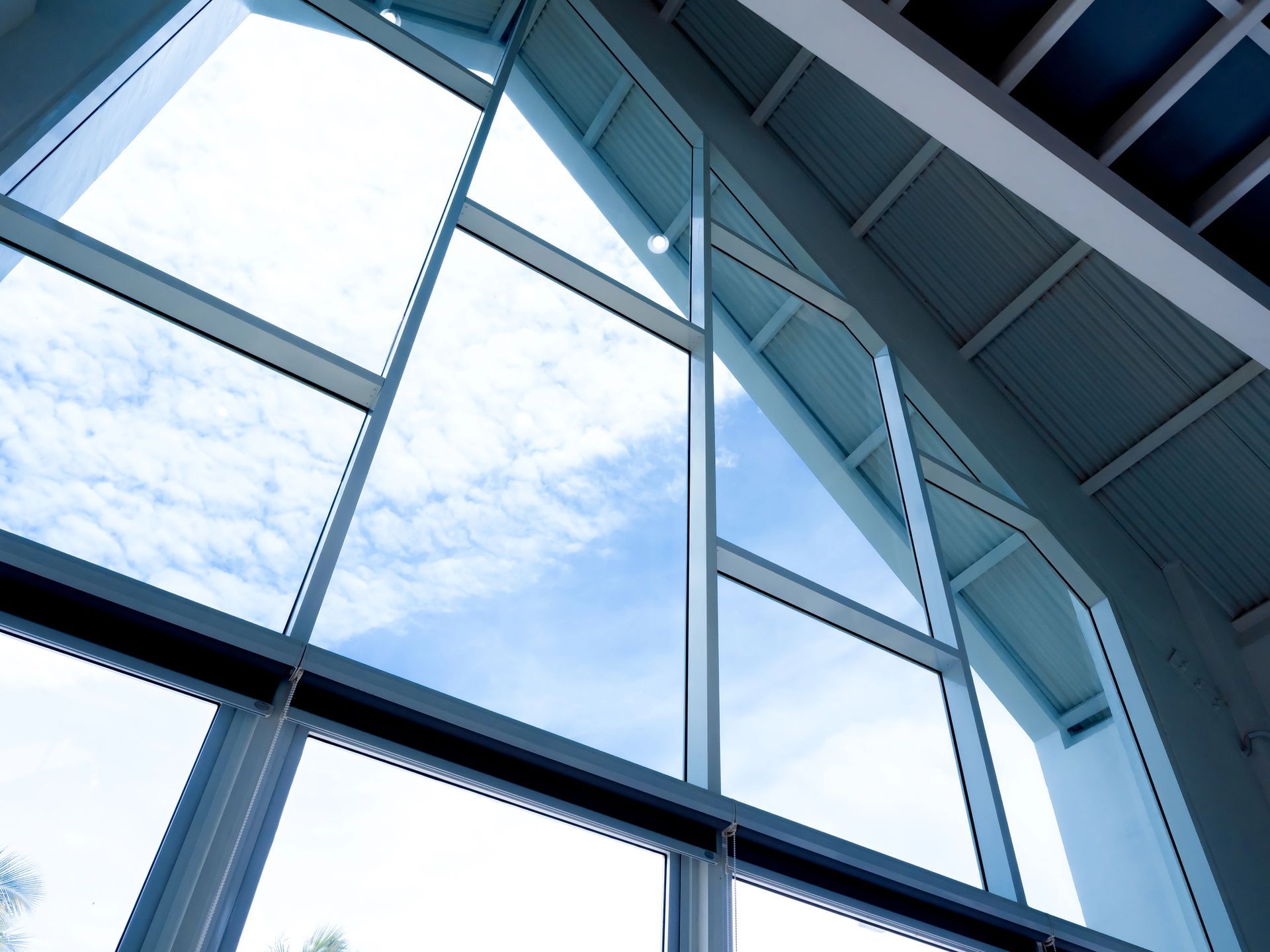 Una vista dal basso di un'ampia finestra triangolare che mostra un cielo azzurro brillante con nuvole leggere, sotto un soffitto bianco.