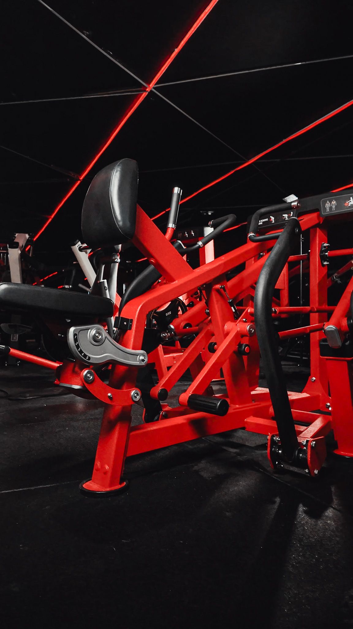 Bicicleta ergométrica vermelha com assento e guidão pretos em um piso escuro de academia, iluminado por detalhes em vermelho.