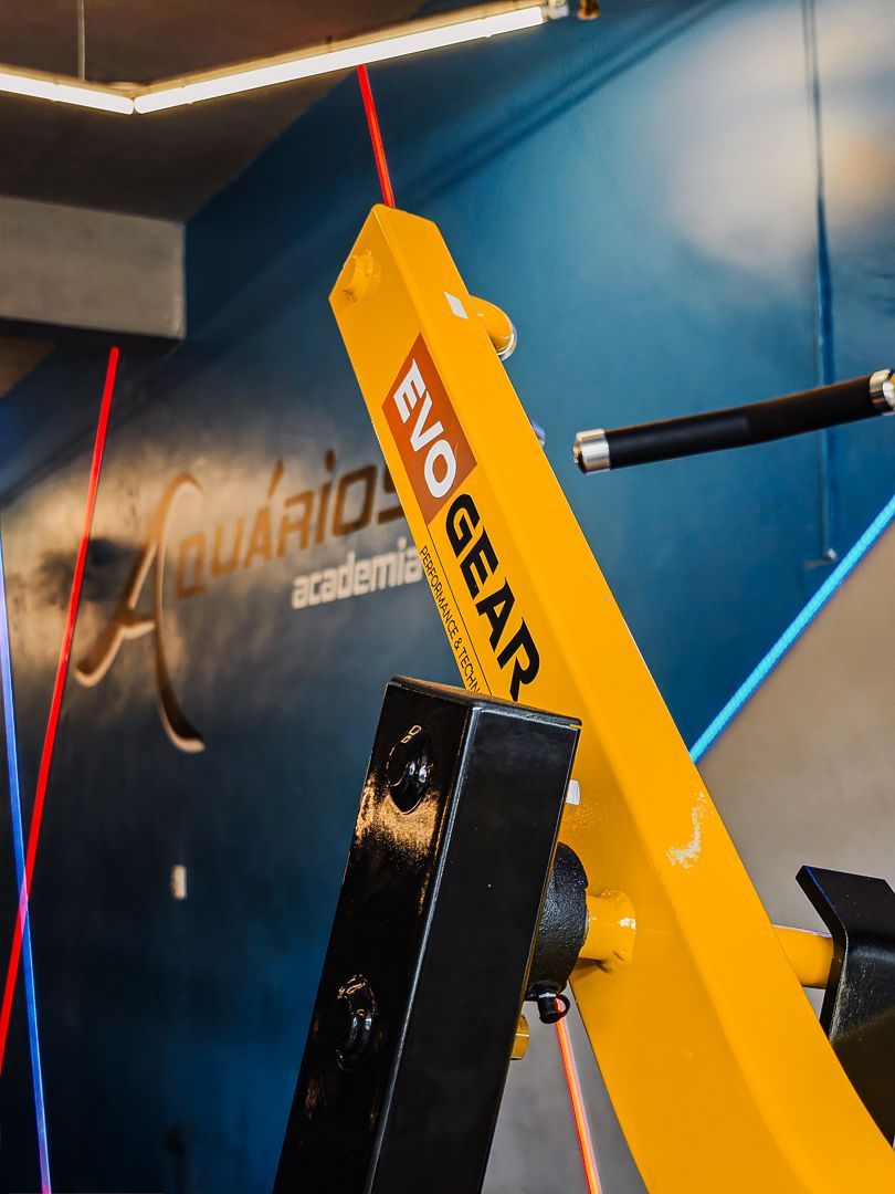 Aparelho de ginástica amarelo da EVOGEAR contra uma parede azul com estofamento preto e cabos vermelhos.