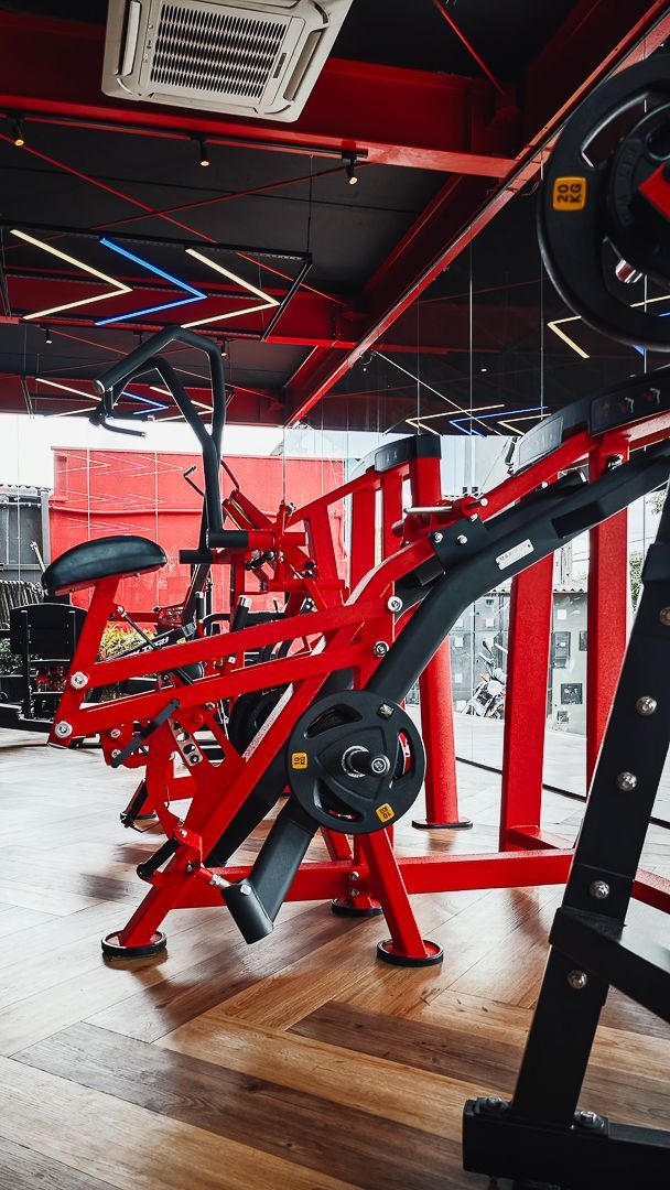 Aparelho de musculação vermelho com suportes pretos em uma sala de ginástica com decoração em vermelho e preto vibrantes.