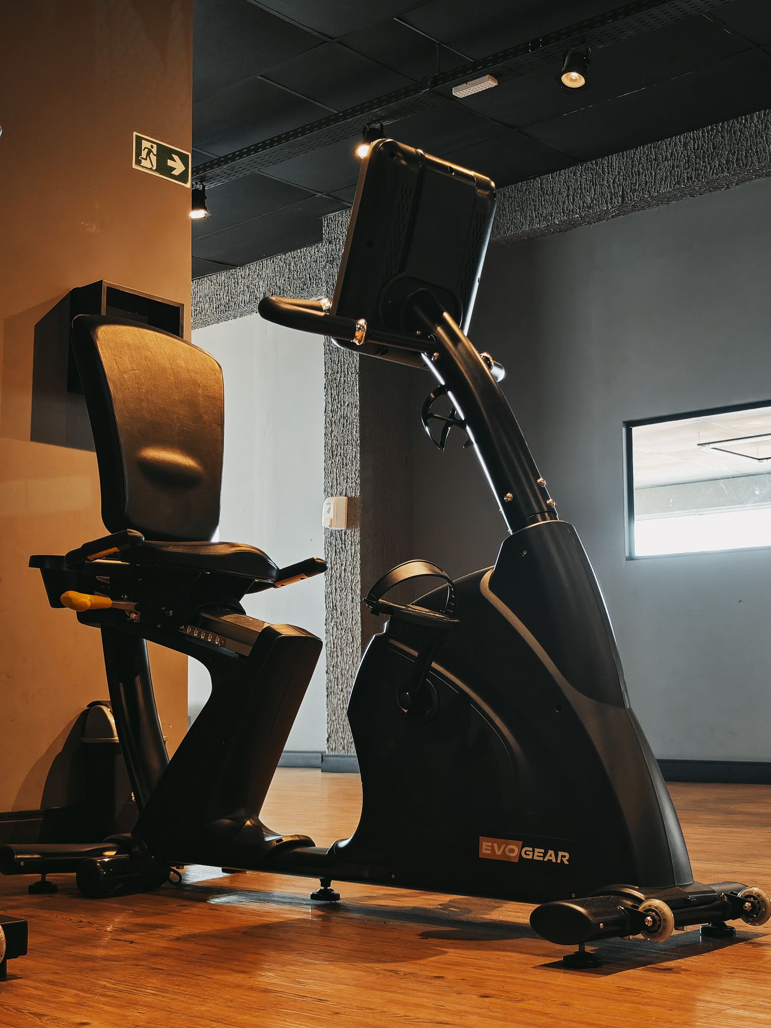 Bicicleta ergométrica estacionária preta em uma academia, com assento acolchoado e painel de controle vertical.