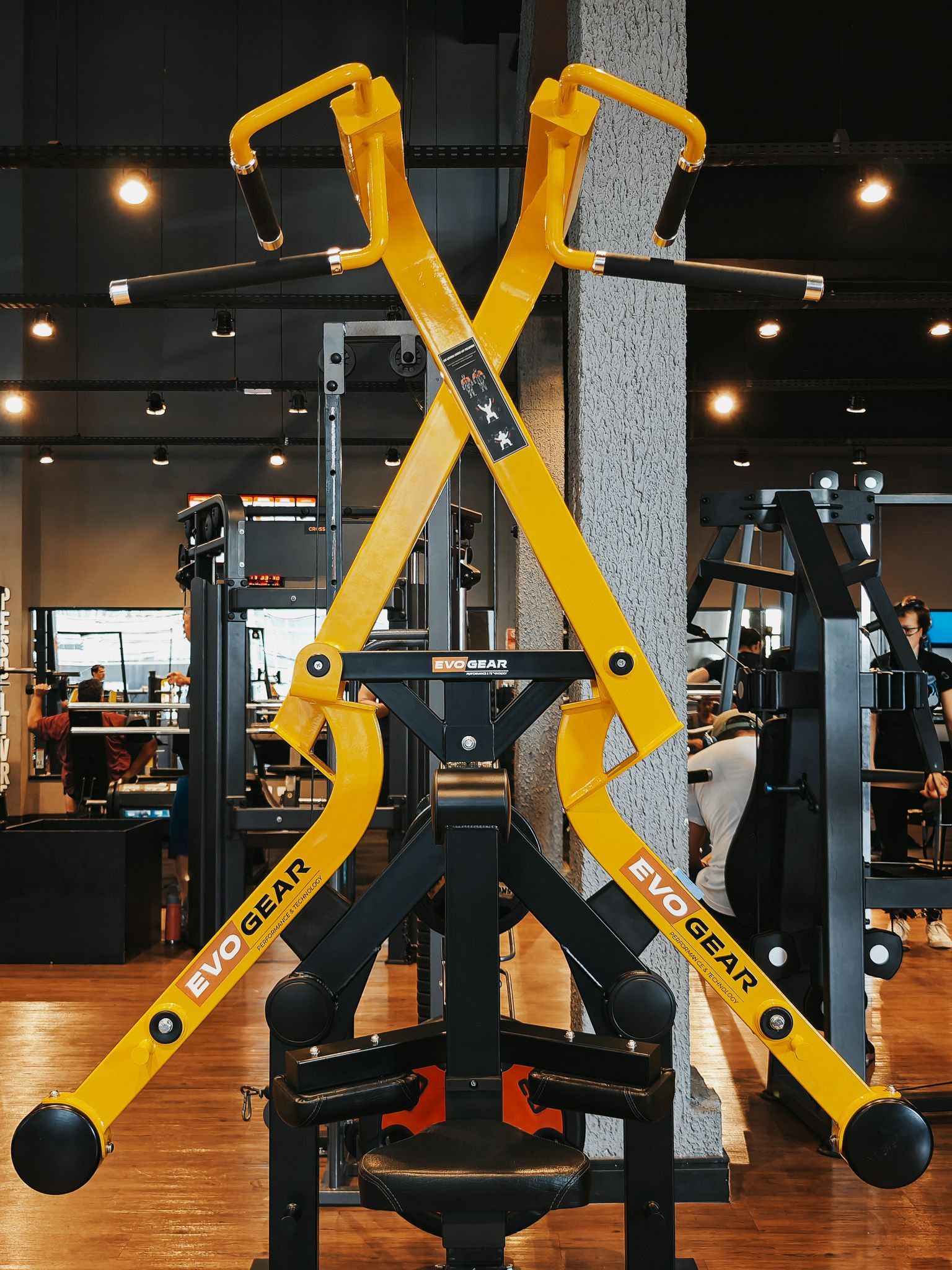 Aparelho de ginástica amarelo XMark em uma academia, dobrado na vertical contra um pilar de concreto.