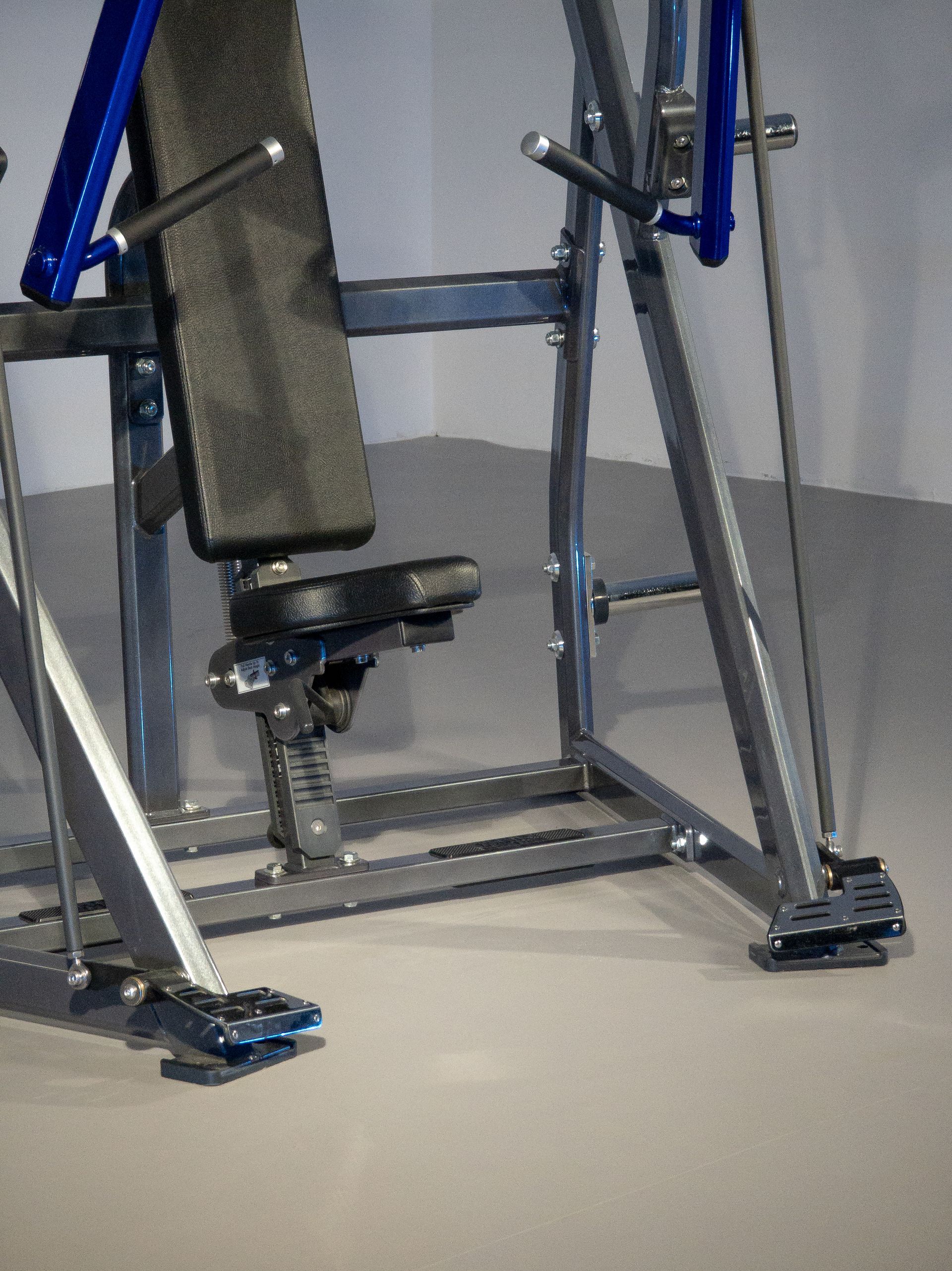 Aparelho de ginástica metálico com assento acolchoado e plataformas para os pés em um ambiente de academia.