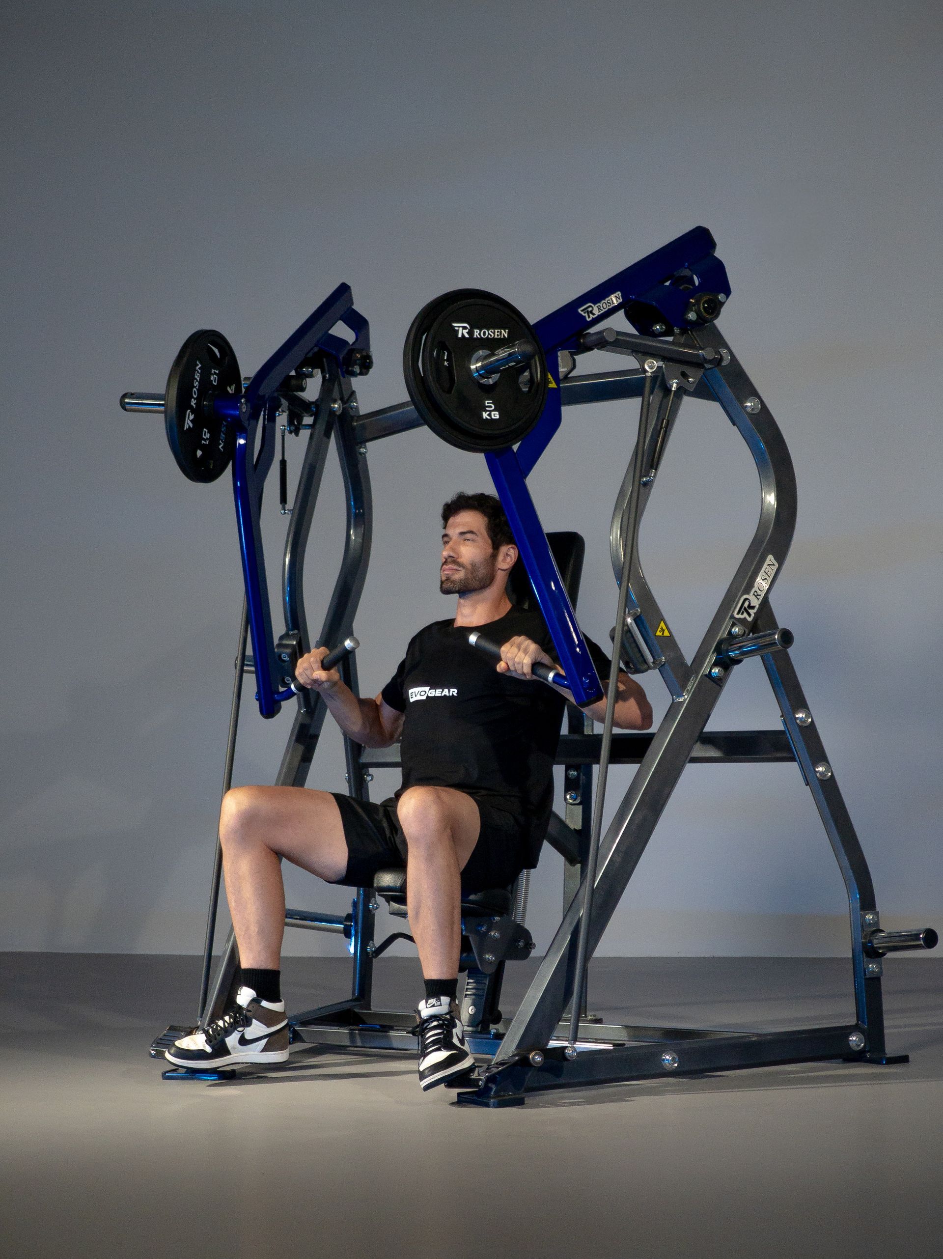 Homem usando uma máquina de leg press sentado em uma academia, com equipamentos azuis e cinzas.
