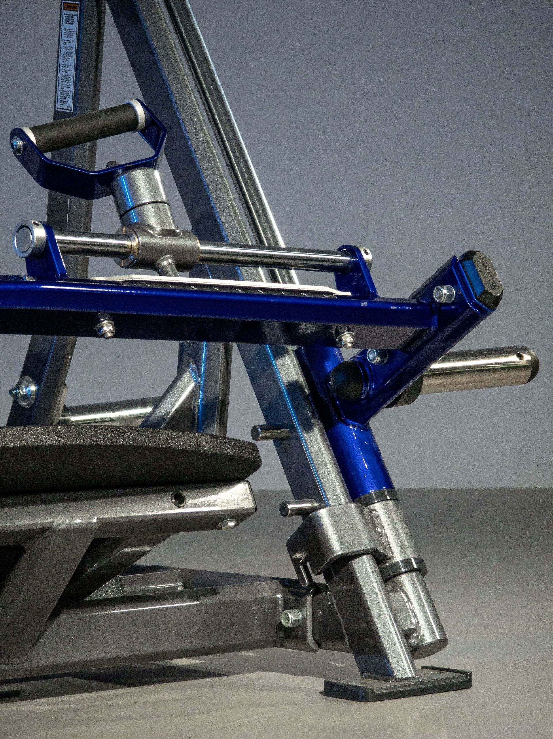Close-up do pedal e da estrutura de uma máquina de exercícios azul e prateada em um ambiente de academia.