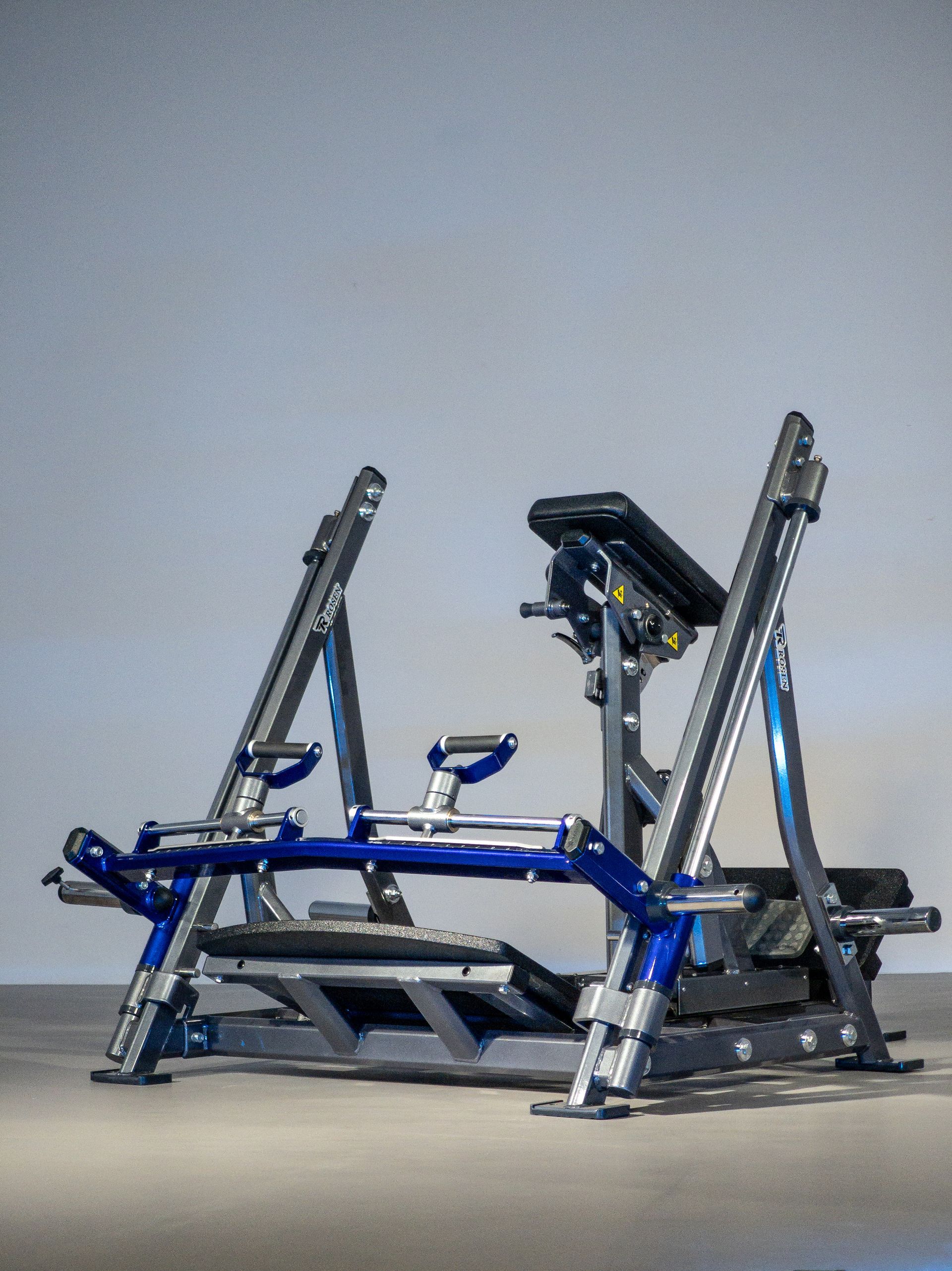 Máquina de leg press azul e prata com trilhos angulares e plataforma para os pés em um fundo cinza de estúdio.