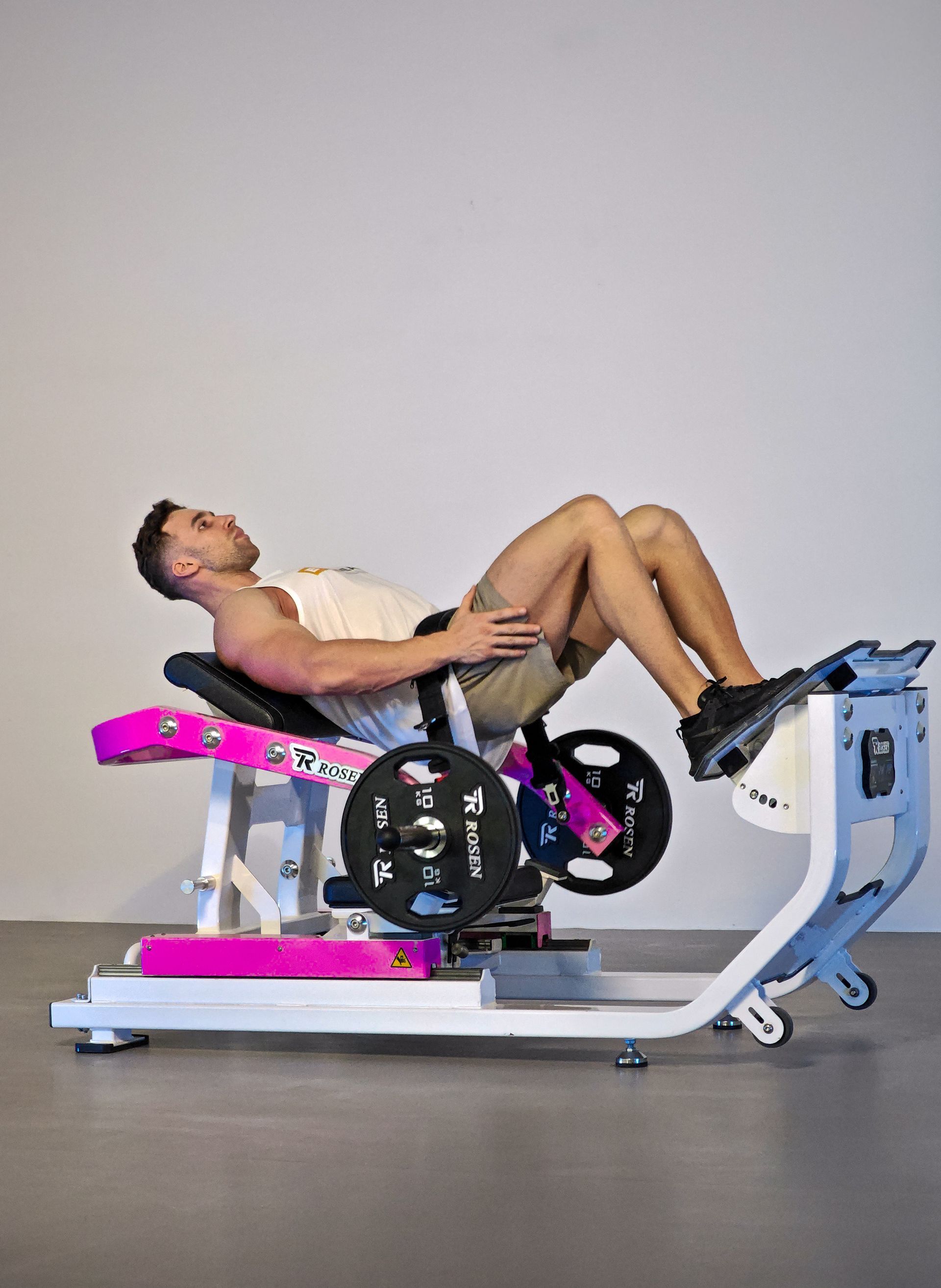 Pessoa se exercitando em uma máquina de leg press em uma academia, inclinada para trás com os joelhos flexionados.