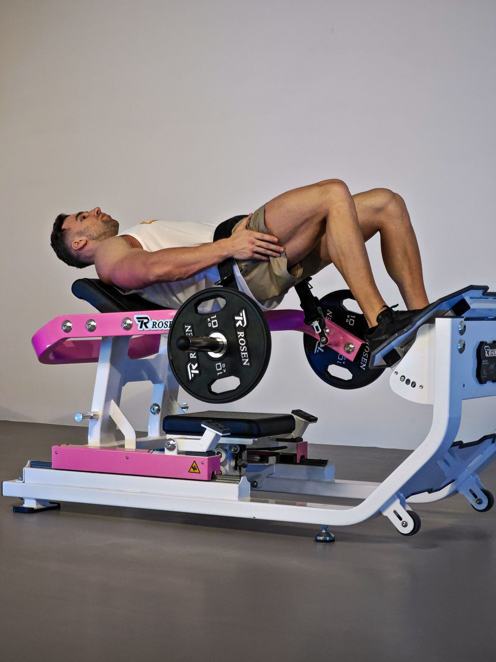Pessoa realizando um exercício de elevação de quadril com barra em um banco de ginástica rosa em um estúdio de fitness.
