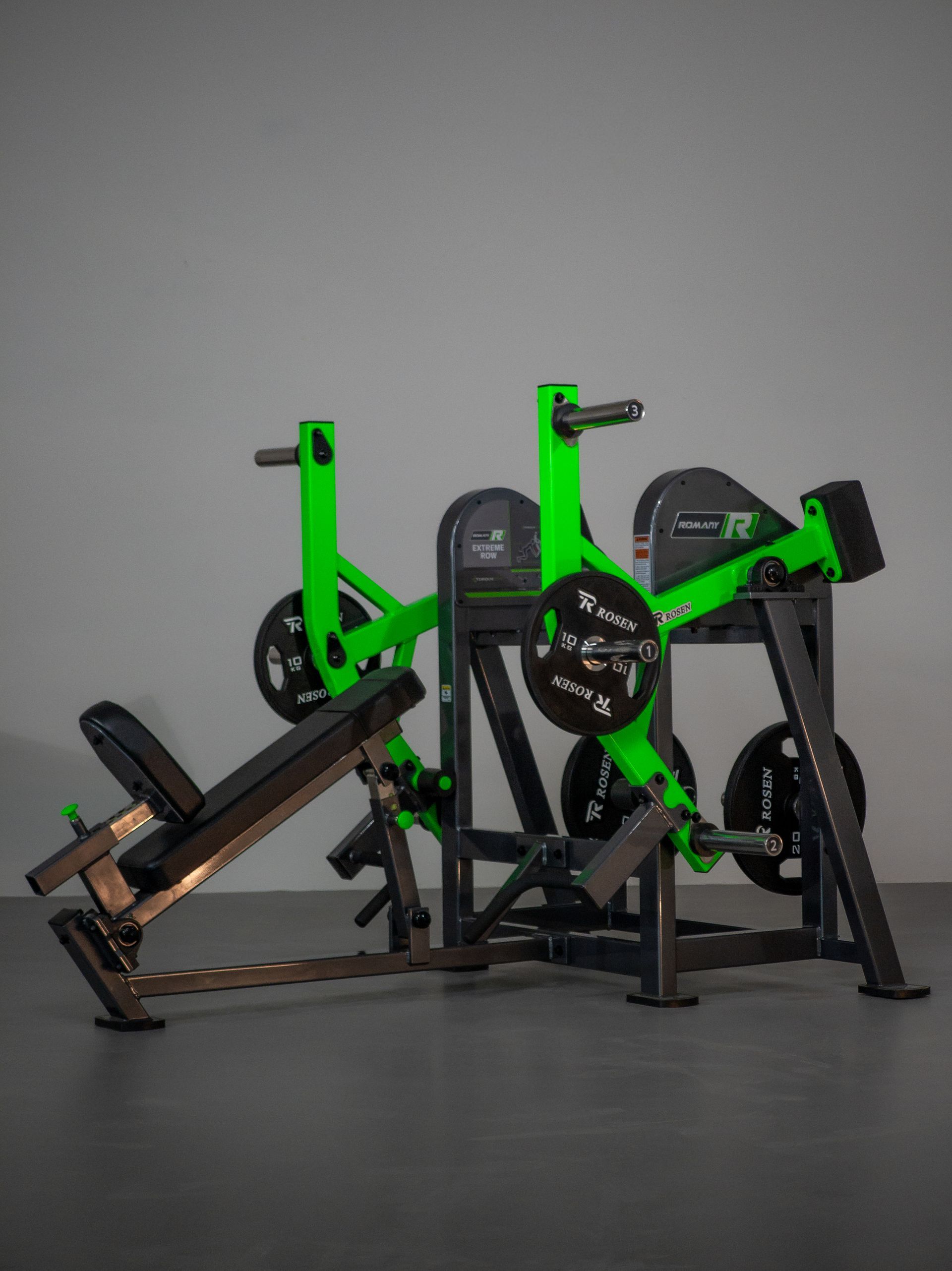 Duas máquinas de leg press verdes e pretas lado a lado em um piso cinza de estúdio.