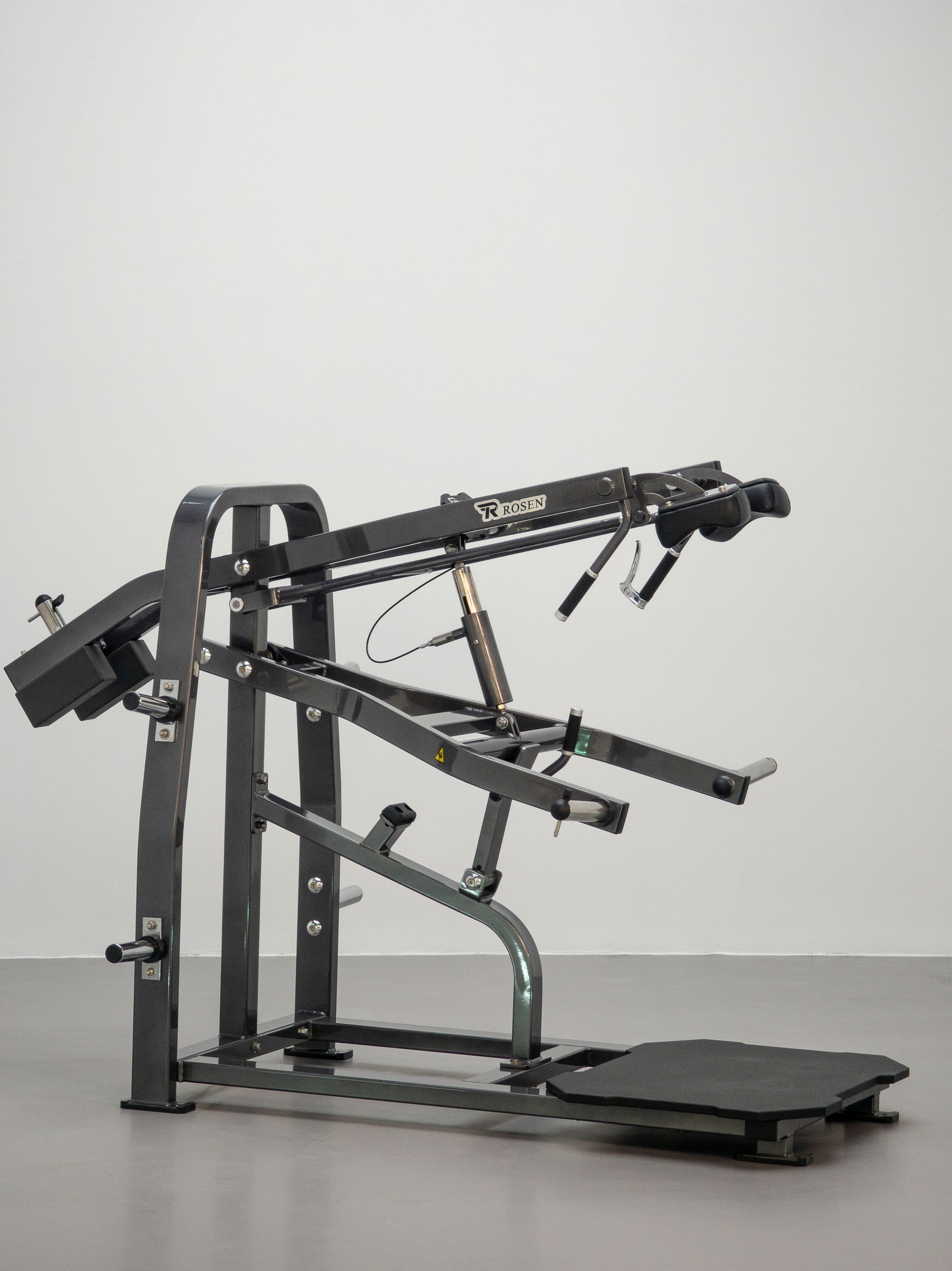 Aparelho de ginástica preto com braços ajustáveis ​​e plataforma para os pés sobre um fundo claro liso.