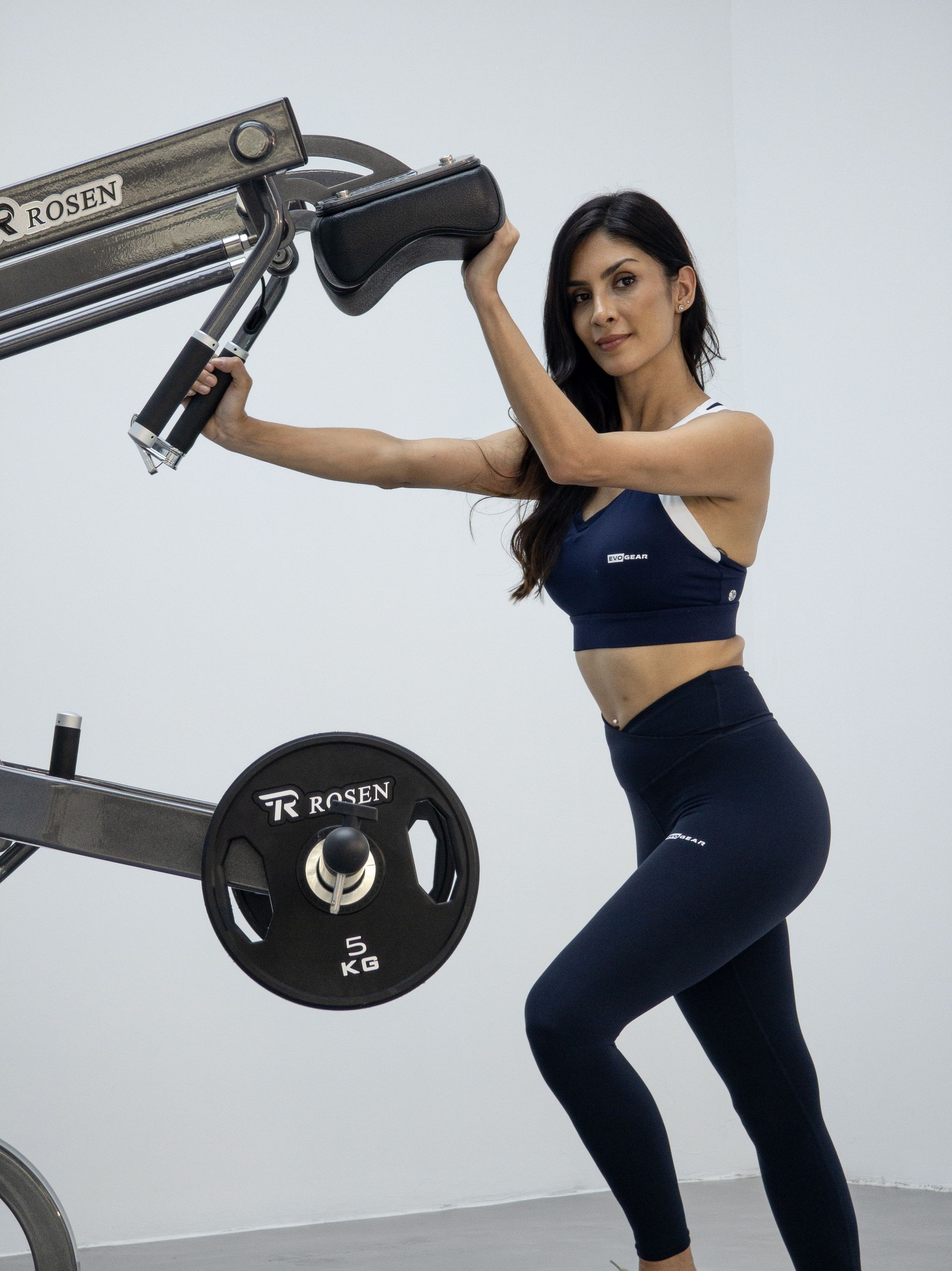 Mulher se exercitando em uma máquina de cabos em uma academia, vestindo roupas de ginástica azul-marinho.