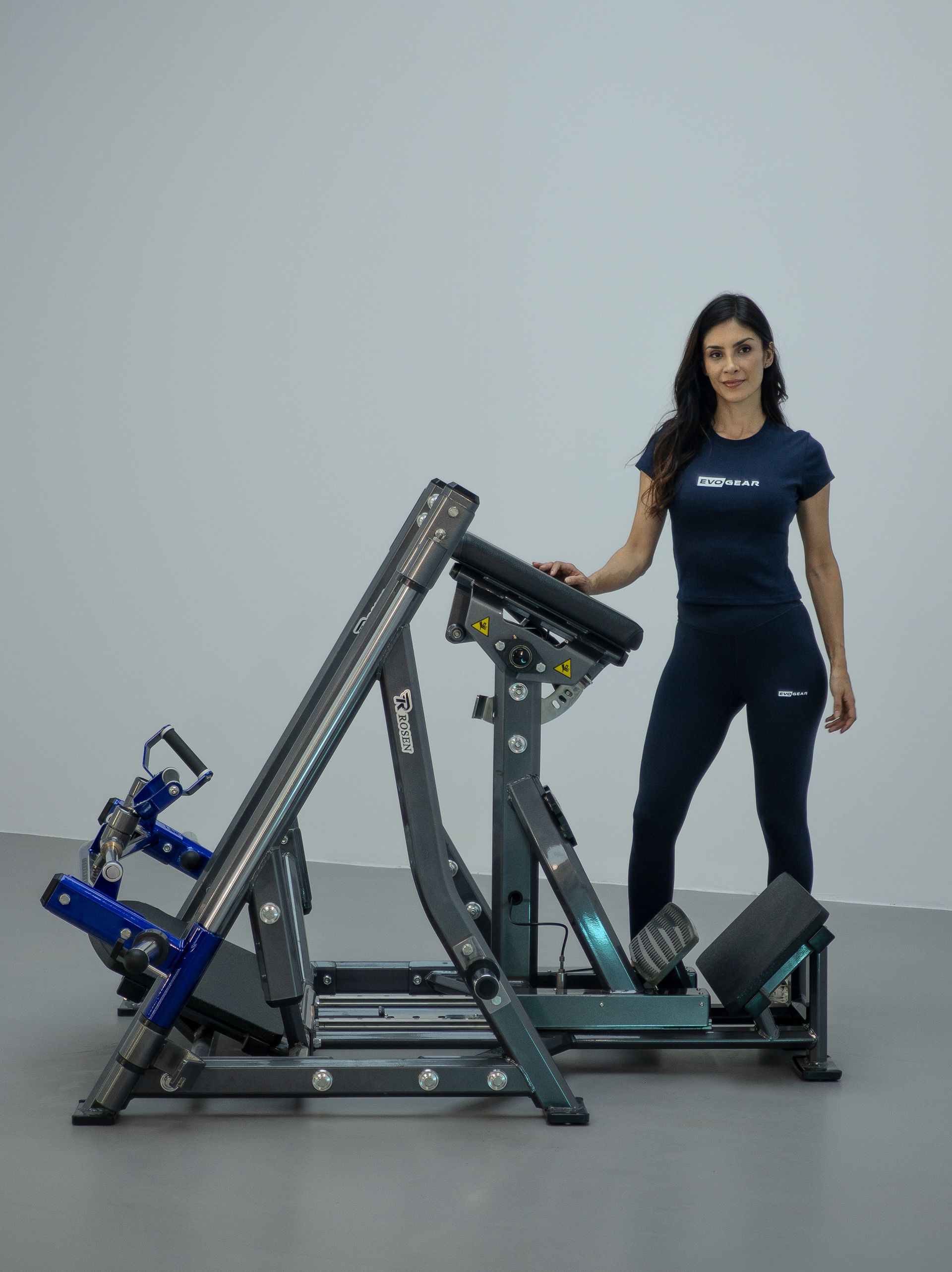 Mulher em pé ao lado de um aparelho de musculação em uma academia, segurando o console.