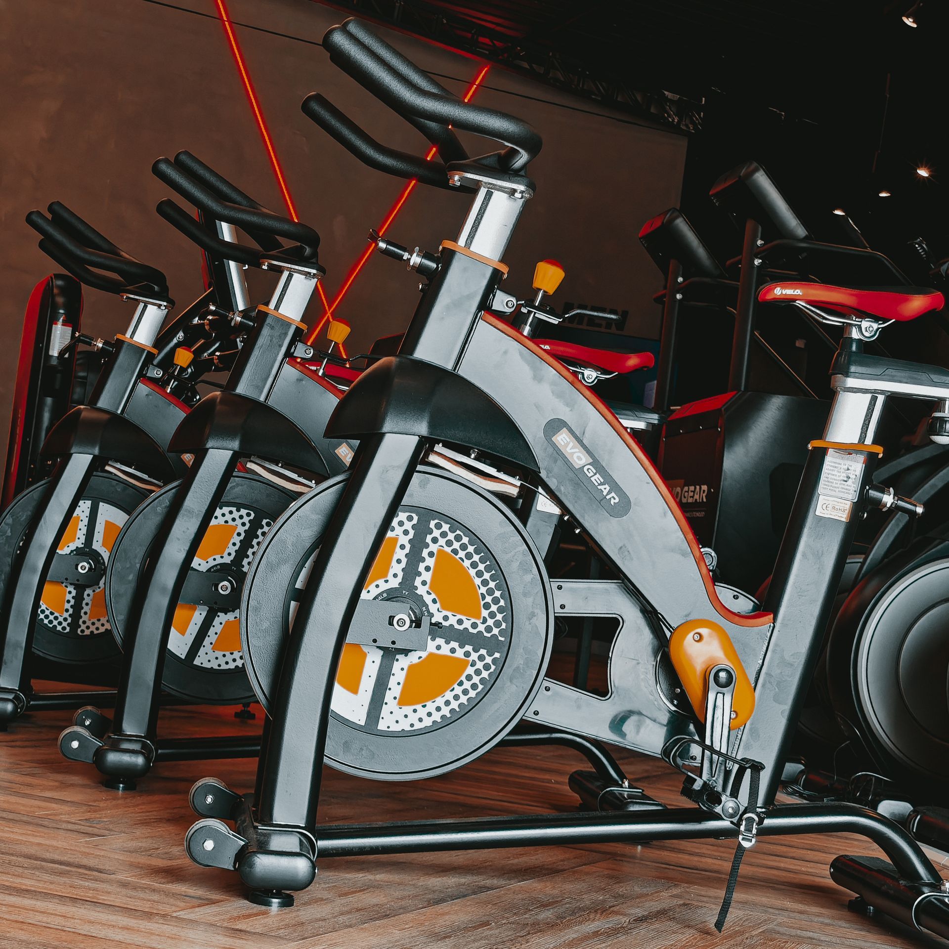 Uma fileira de bicicletas ergométricas estão alinhadas em uma academia.