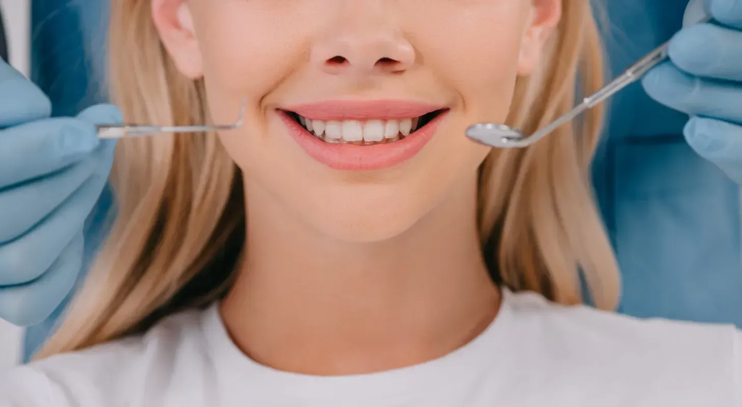 A patient smiling while a dentist wearing blue gloves uses a dental mirror and explorer for an oral examination.