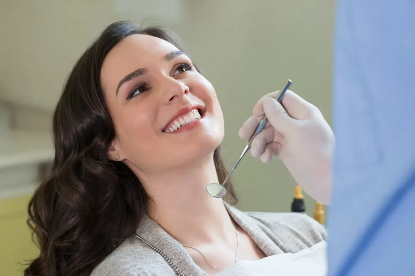 A patient smiling at a dentist who is holding a dental mirror during an examination.