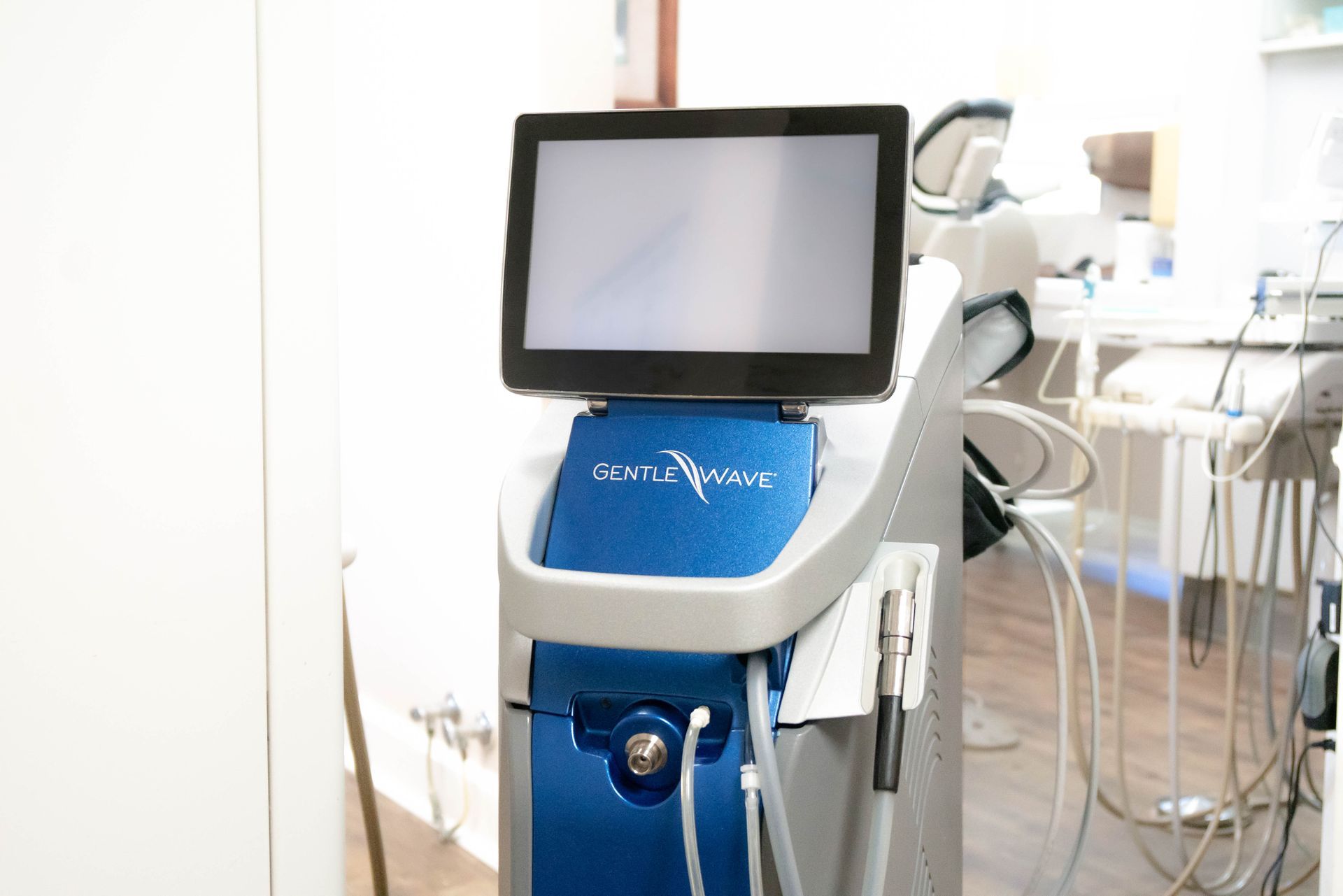 A blue and grey medical laser machine with a touchscreen monitor, positioned in a dental office.