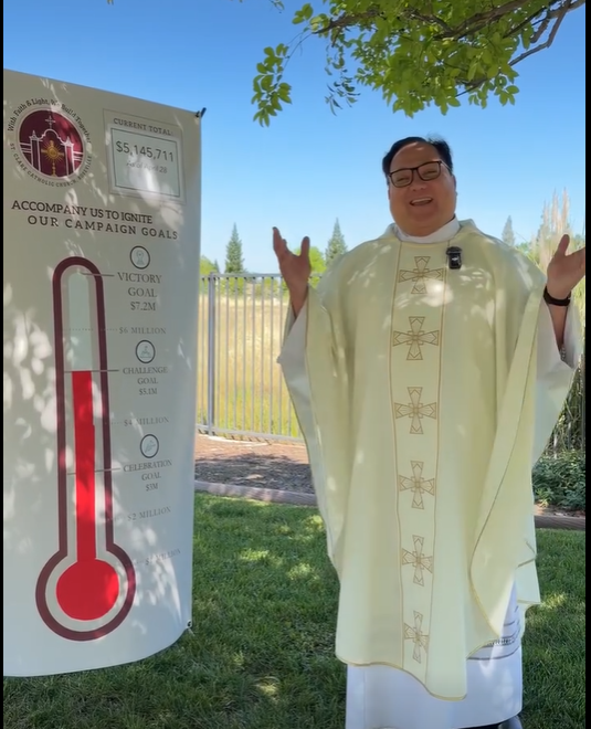 Fr. George standing next to the Campaign Goals/Totals poster