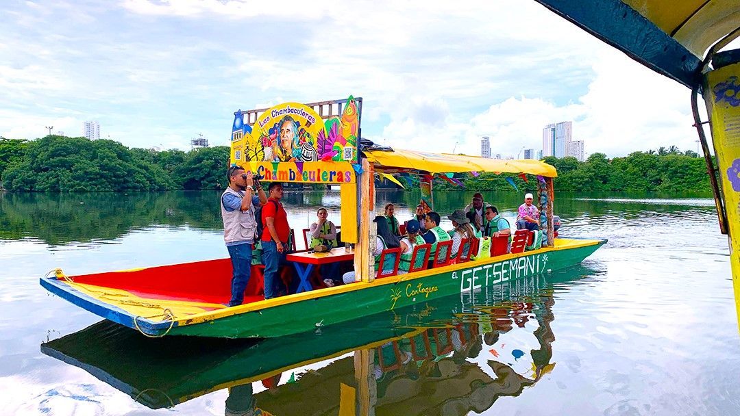 A colorful boat with passengers on a lake, surrounded by green trees.