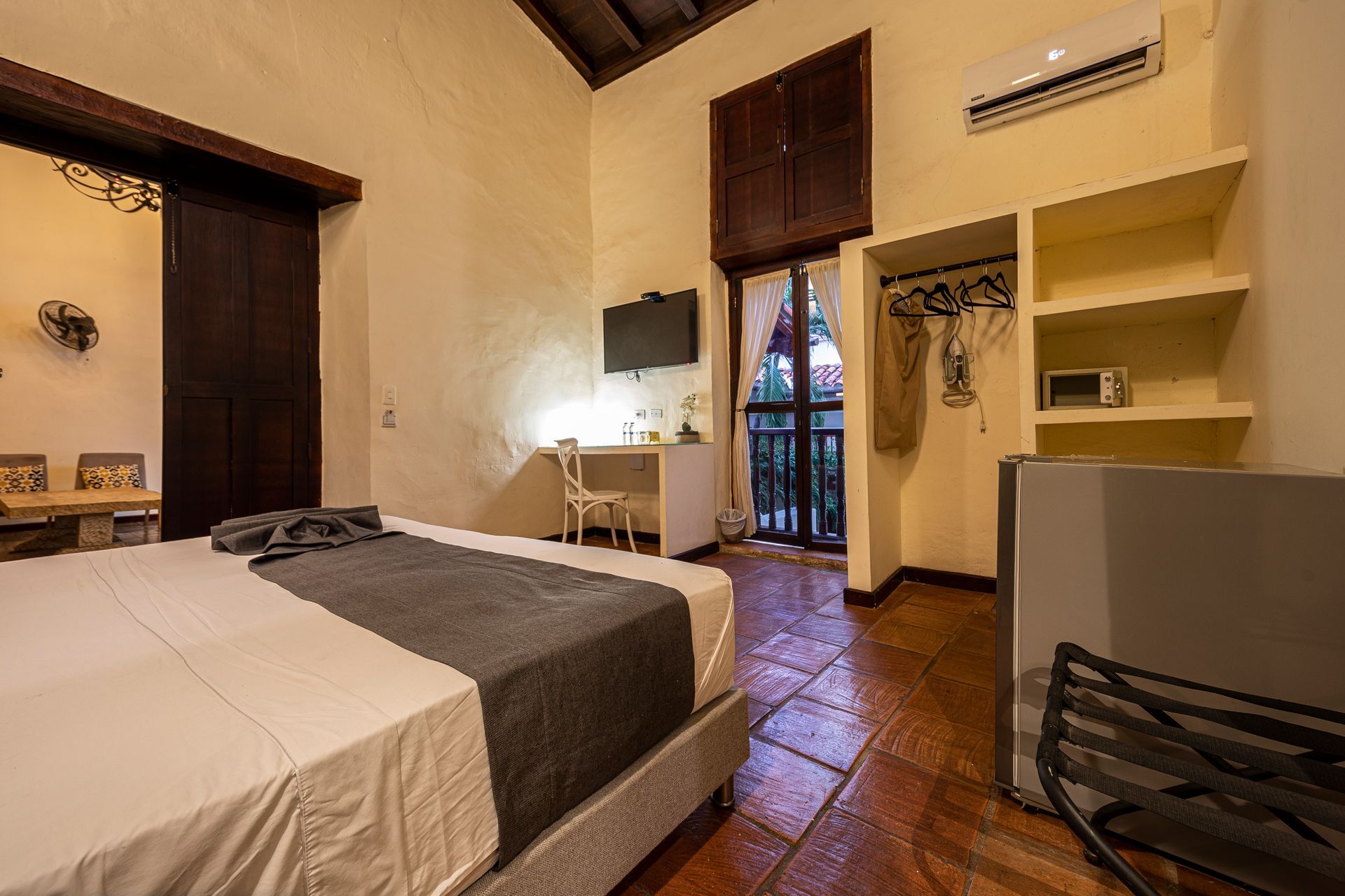 A hotel room with a king size bed , a desk , a refrigerator and a balcony.
