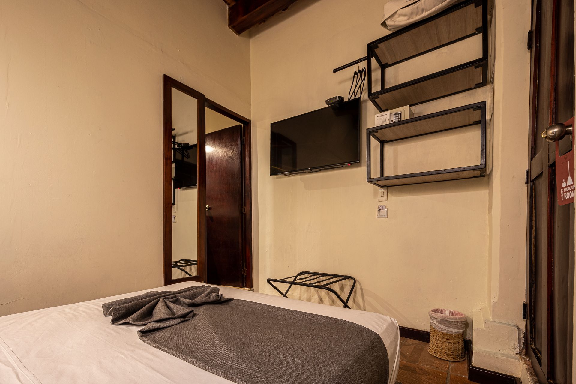 A bedroom with a bed , television , mirror and shelves.