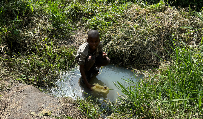 young boy is kneeling in a puddle of water