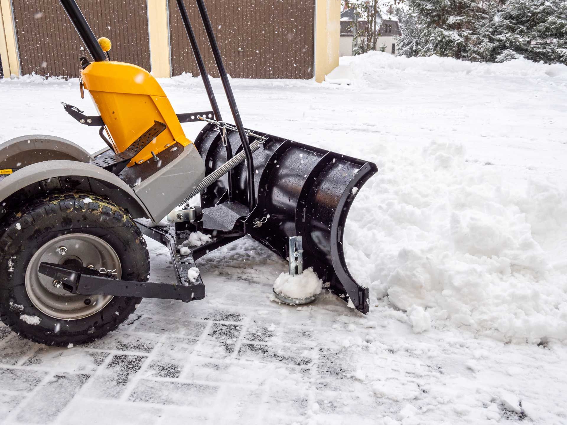 Yellow snow plow clearing snow from a paved driveway. Yellow snow plow clearing snow from a paved driveway.