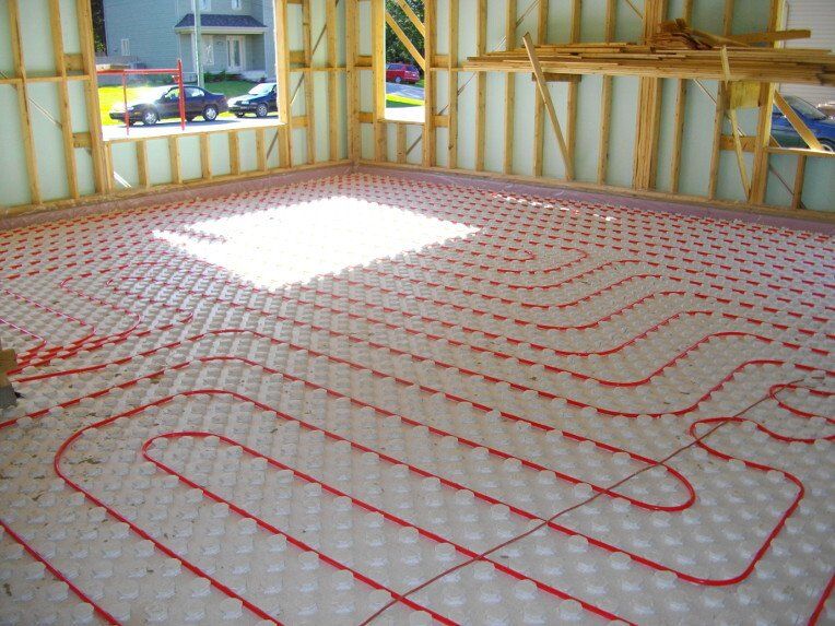 Tuyaux rouges d'un système de chauffage par le sol radiant installé sur l'isolant d'un bâtiment en construction.