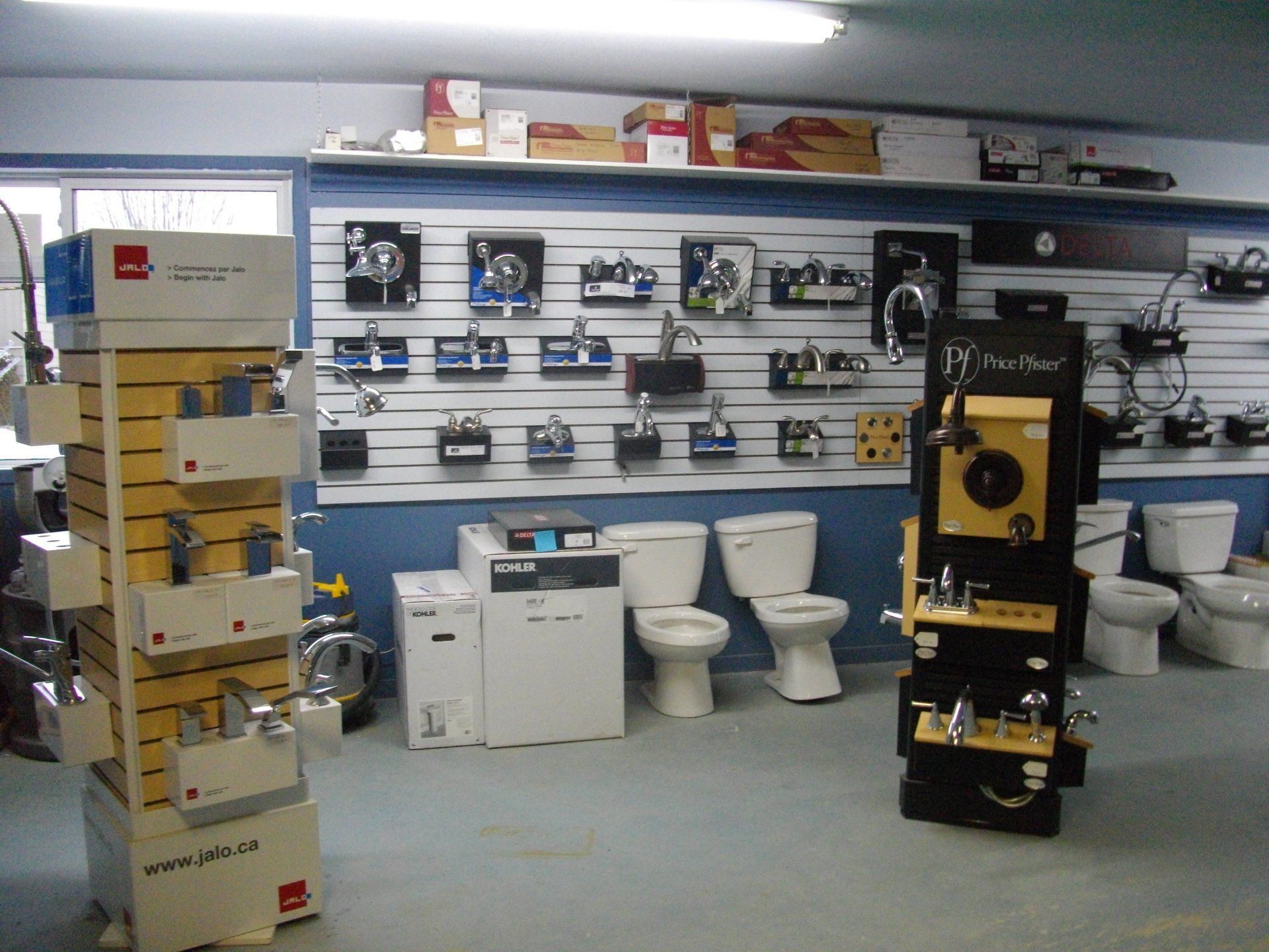 Intérieur d'un magasin de fournitures de plomberie avec présentoirs de robinetterie, toilettes et une palette de couleurs blanche, bleue et grise.
