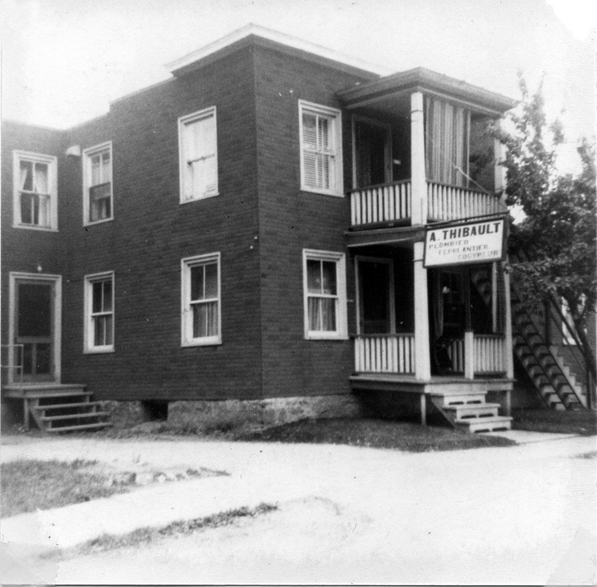 Bâtiment en briques de deux étages avec un porche, une enseigne indiquant « A. Thibault ».
