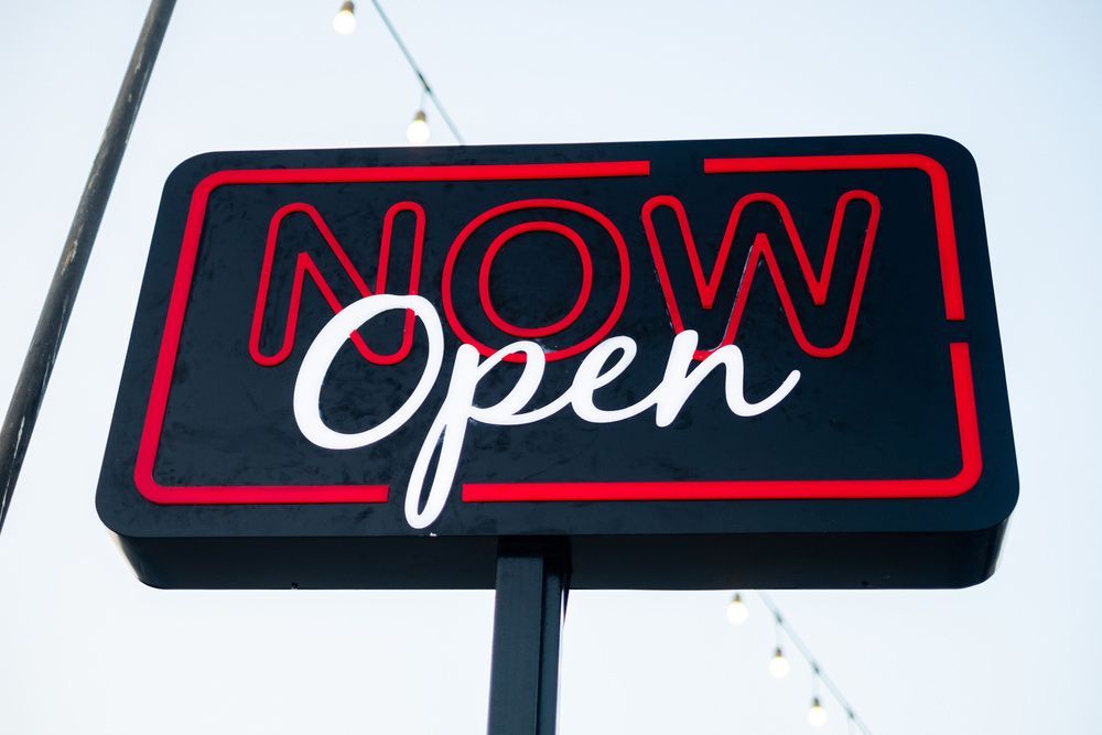A Neon Sign That Says  Now Open is Hanging From a Pole — Cairns Synergy Electrical in Manunda, QLD