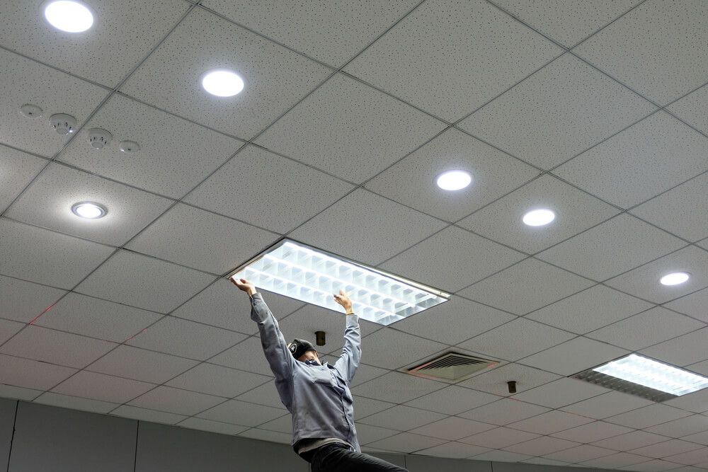 A Man is Hanging From the Ceiling While Holding a Light — Cairns Synergy Electrical in Manunda, QLD