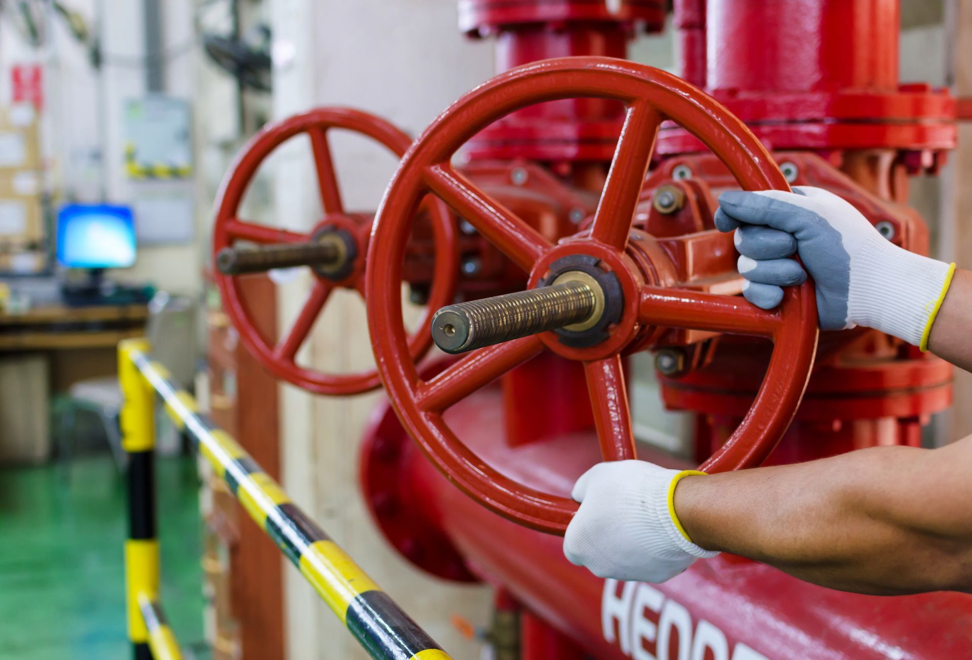 Person in blue uniform inspecting a red fire extinguisher, holding a clipboard, in a room with other fire extinguishers. Hands in white gloves turn a red valve wheel on industrial piping.