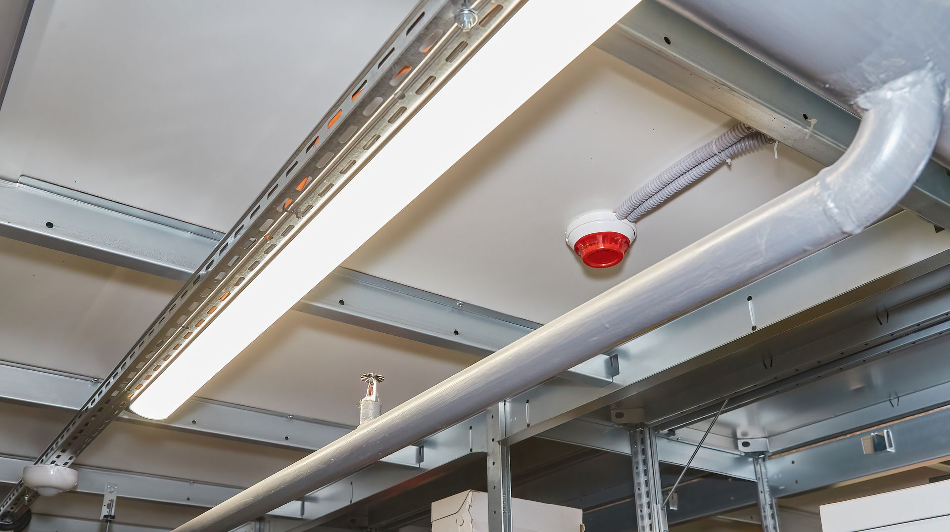 Ceiling with a long light, pipes, and a smoke detector.