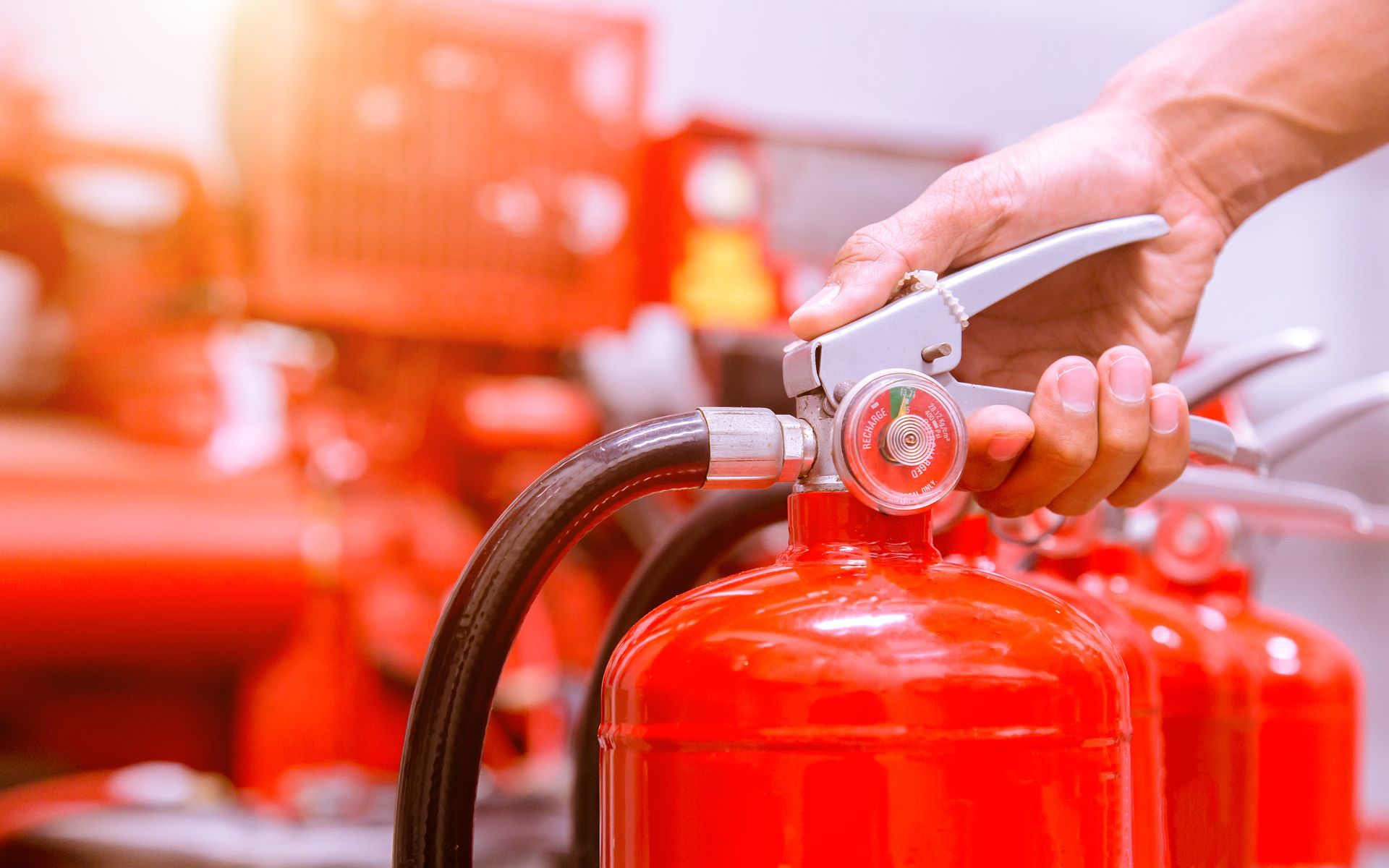 Hand holding a fire extinguisher handle, nozzle aimed, in a red-themed setting. Hand holding a fire extinguisher handle, nozzle aimed, in a red-themed setting.
