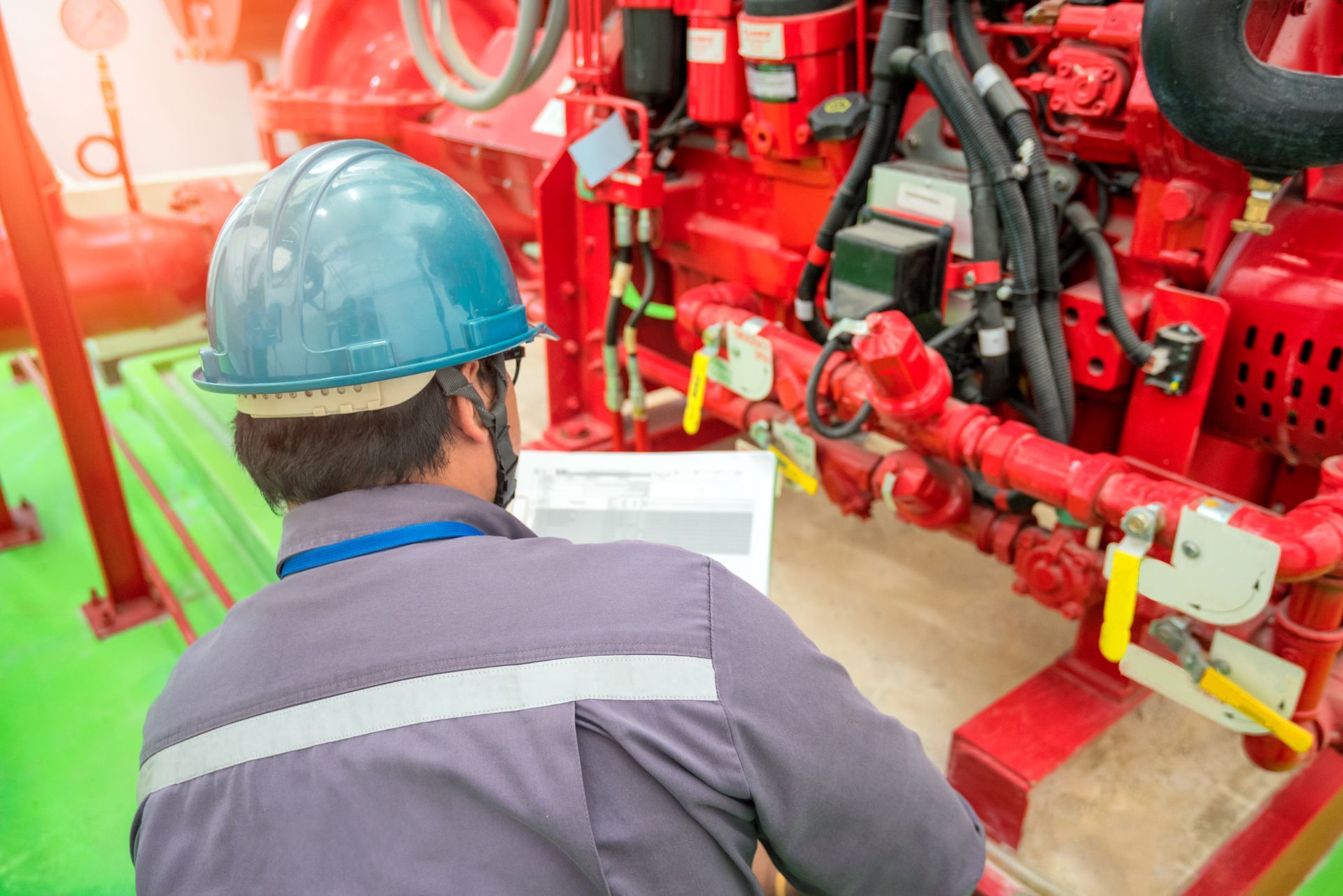 Person in blue hard hat inspecting red machinery, holding a document. Person in blue hard hat inspecting red machinery, holding a document.